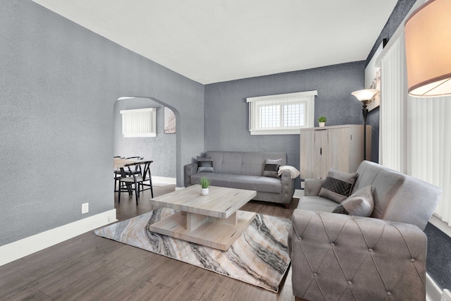 living area with arched walkways, wood finished floors, a textured wall, and baseboards