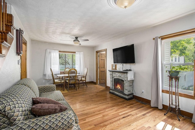 living area featuring light wood-style floors, a fireplace, baseboards, and a ceiling fan