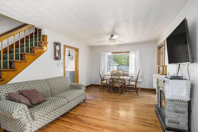 living area featuring light wood finished floors, stairs, ceiling fan, baseboards, and a glass covered fireplace