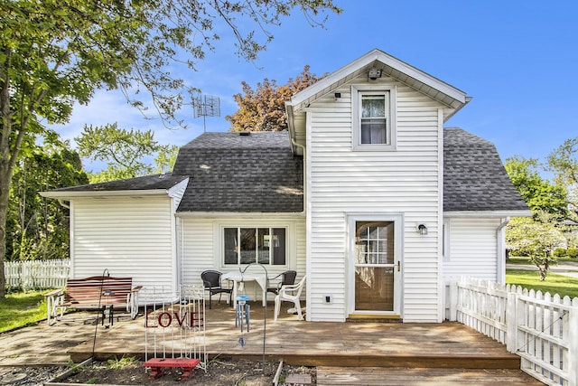 rear view of house featuring a shingled roof, a deck, and fence