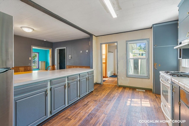 kitchen featuring white range with gas cooktop, light countertops, freestanding refrigerator, dark wood-type flooring, and under cabinet range hood