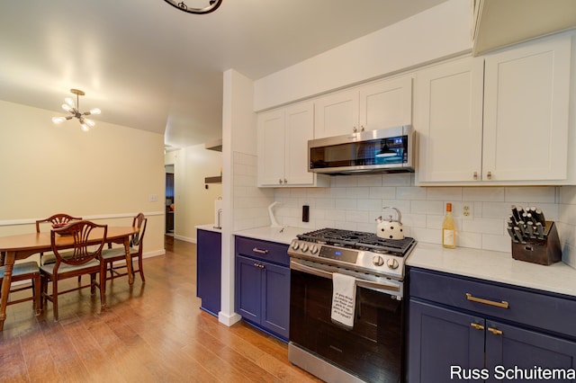 1572 Cornell Rd, Muskegon, MI 49441 - kitchen with stainless steel appliances, blue cabinetry, a chandelier, decorative backsplash, and light wood-style floors