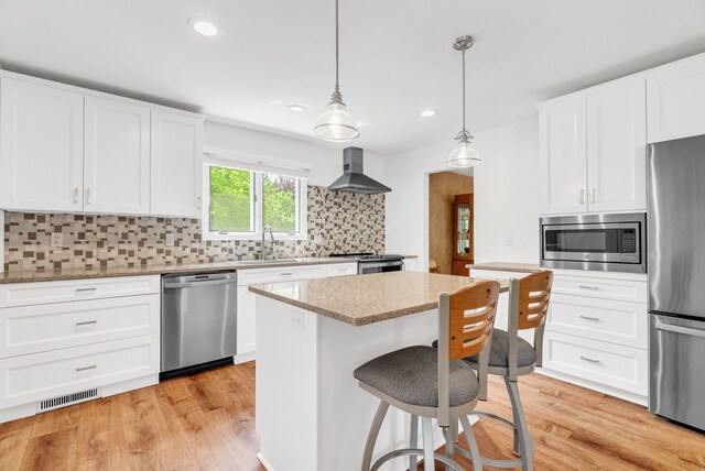 836 Boutell Dr, Grand Blanc, MI 48439 - kitchen featuring stainless steel appliances, wall chimney exhaust hood, a sink, a kitchen island, and light stone countertops