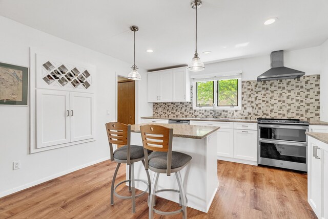 836 Boutell Dr, Grand Blanc, MI 48439 - kitchen featuring wall chimney range hood, appliances with stainless steel finishes, white cabinetry, tasteful backsplash, and a center island