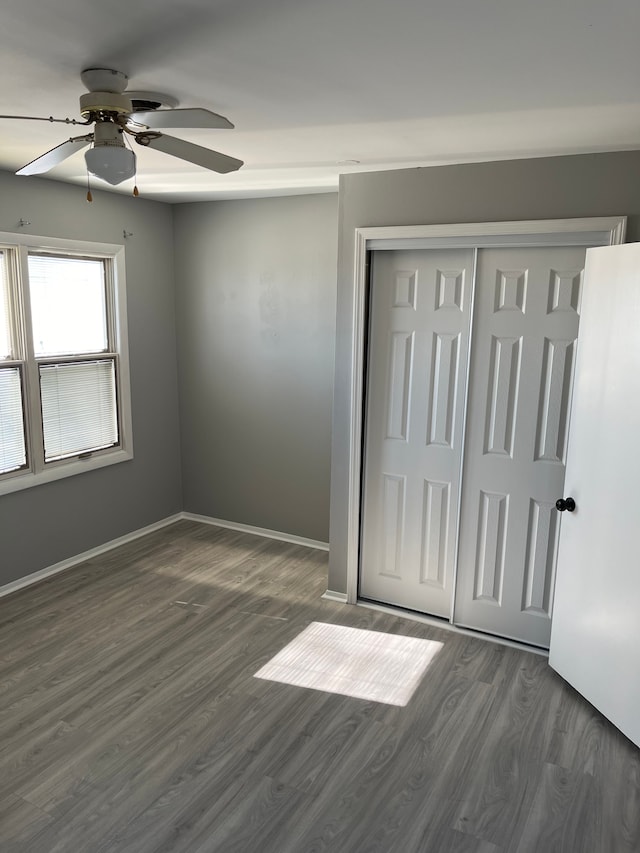 unfurnished bedroom with dark wood-style flooring, a closet, baseboards, and ceiling fan