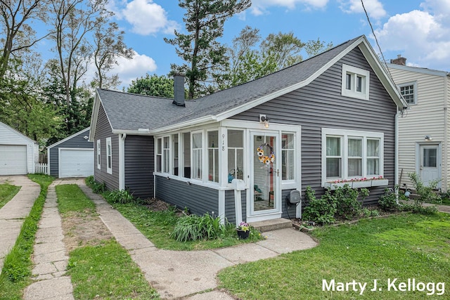 bungalow-style home featuring a chimney, a front lawn, a garage, roof with shingles, and an outbuilding