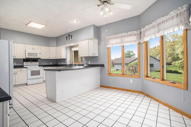 kitchen with white appliances, a peninsula, white cabinetry, dark countertops, and a ceiling fan
