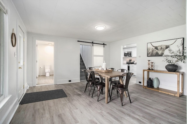 dining area featuring a barn door, light wood-style flooring, and baseboards