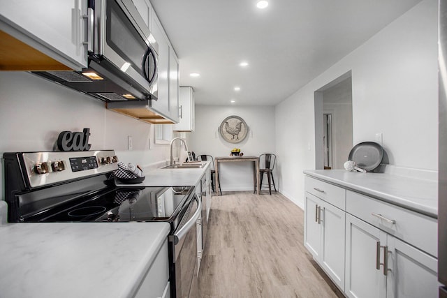 kitchen featuring appliances with stainless steel finishes, a sink, light wood-type flooring, light countertops, and recessed lighting