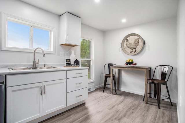 kitchen with a sink, white cabinets, light wood-type flooring, light countertops, and recessed lighting