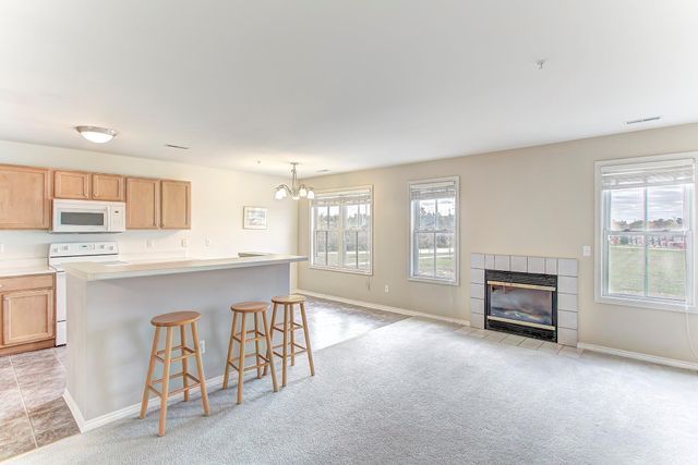 3986 Forester Blvd, Auburn Hills, MI 48326 - kitchen featuring white appliances, a chandelier, light colored carpet, a fireplace, and a kitchen bar