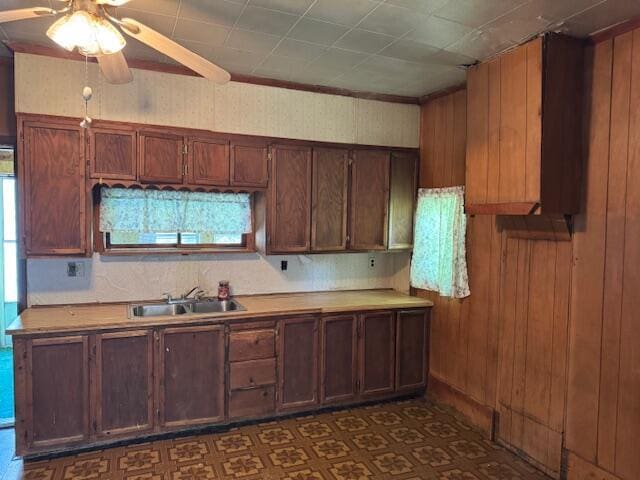kitchen with a sink, a ceiling fan, light countertops, and wooden walls