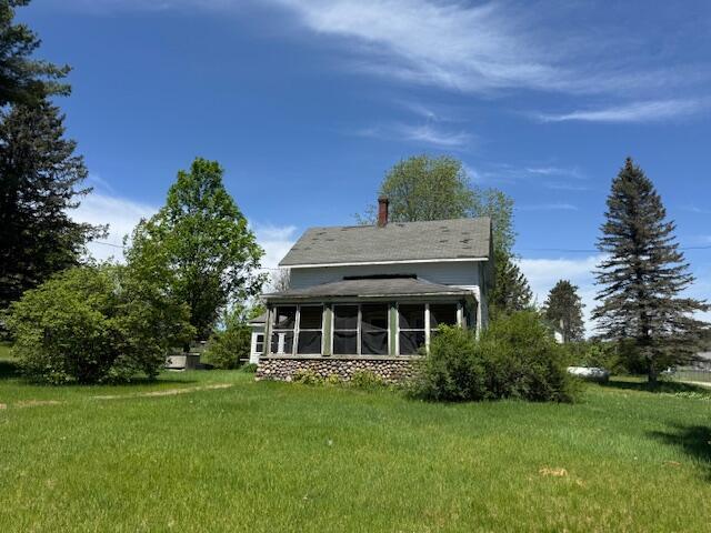 back of property with a sunroom, a lawn, and a chimney