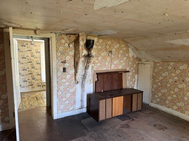 bonus room featuring lofted ceiling, baseboards, dark wood-type flooring, and wallpapered walls