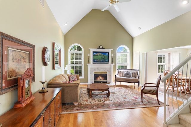 living room with high vaulted ceiling, ceiling fan, stairway, a glass covered fireplace, and light wood-style flooring