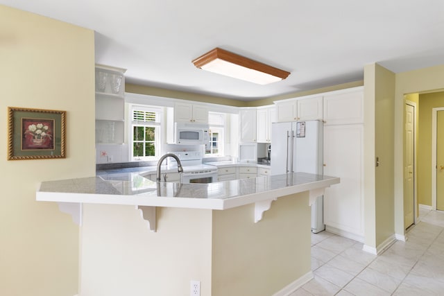kitchen with white appliances, a peninsula, tile countertops, a kitchen bar, and open shelves
