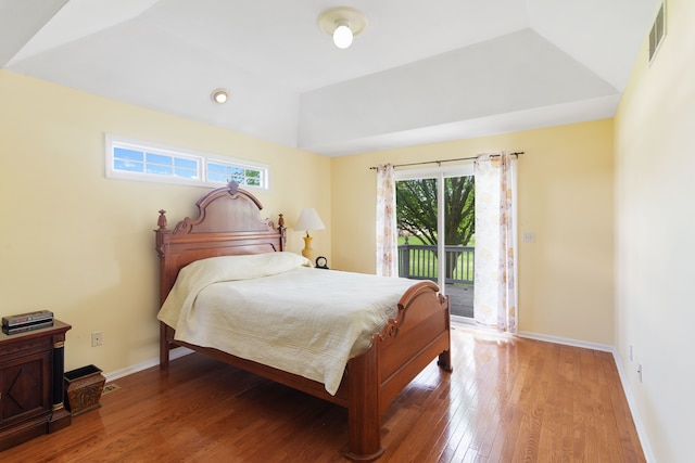bedroom with access to exterior, wood finished floors, baseboards, and a raised ceiling