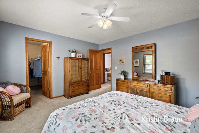 bedroom featuring light colored carpet, a walk in closet, a textured ceiling, ceiling fan, and a closet