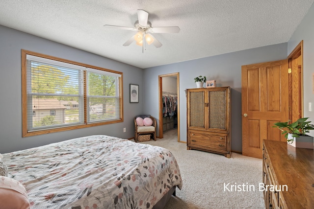 bedroom featuring a spacious closet, a textured ceiling, light colored carpet, a closet, and ceiling fan