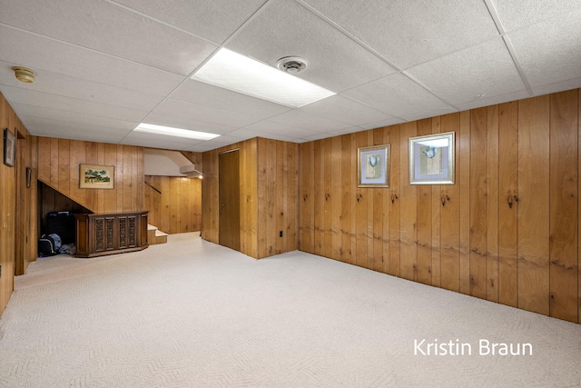 finished basement with carpet flooring, wooden walls, and a paneled ceiling