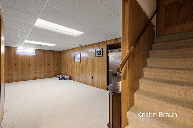 basement featuring wooden walls, stairway, a drop ceiling, and carpet