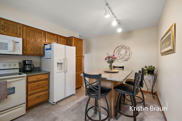 kitchen with white appliances, brown cabinetry, a kitchen breakfast bar, a textured ceiling, and light countertops