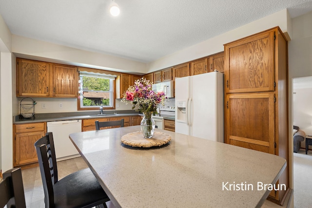 kitchen featuring white appliances, a sink, brown cabinetry, and a kitchen breakfast bar