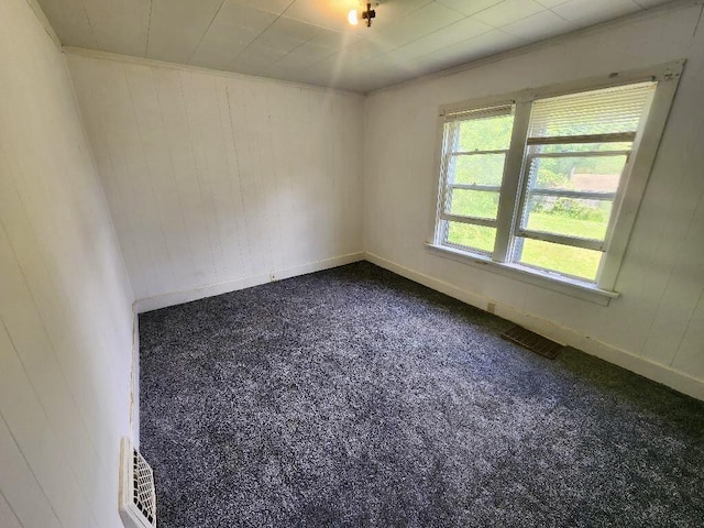 unfurnished room featuring baseboards, wooden walls, ornamental molding, and dark carpet