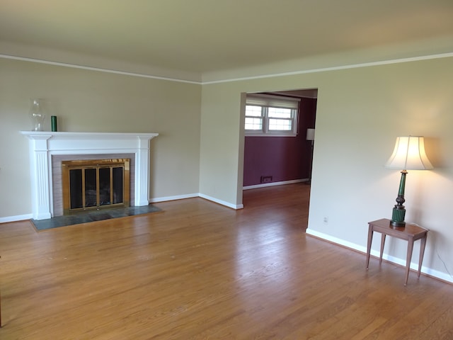 unfurnished living room featuring baseboards, a glass covered fireplace, wood finished floors, and ornamental molding