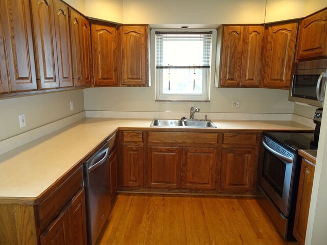 kitchen featuring stainless steel appliances, a sink, brown cabinets, and light countertops