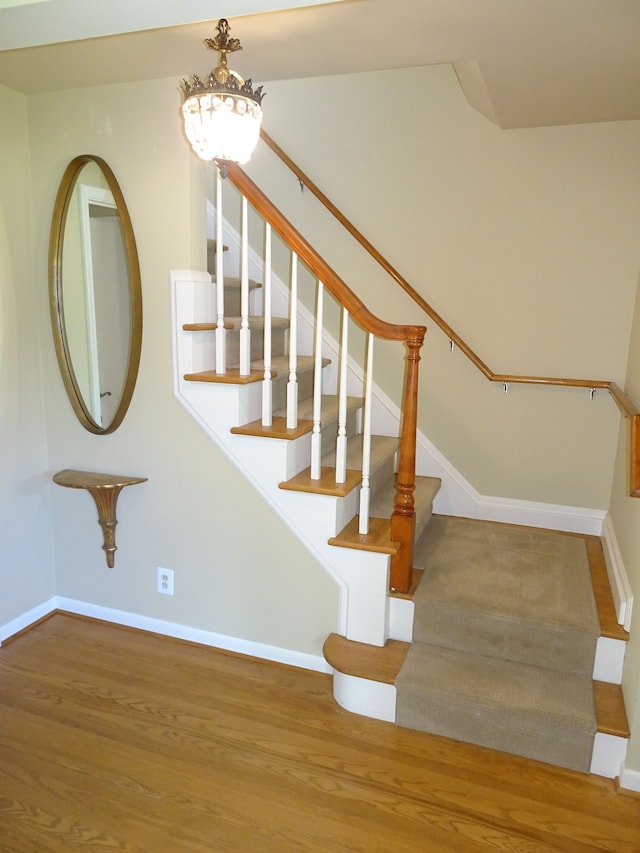 stairway with wood finished floors, baseboards, and a chandelier