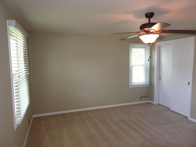 spare room featuring a ceiling fan, light colored carpet, and baseboards