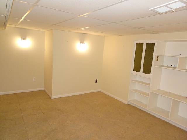unfurnished room featuring a paneled ceiling, baseboards, and built in shelves