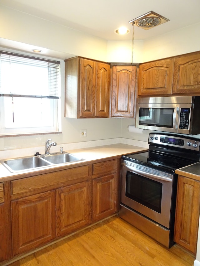 kitchen with stainless steel appliances, brown cabinets, a sink, light wood-style floors, and light countertops