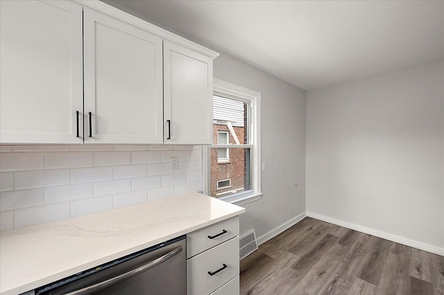kitchen featuring stainless steel dishwasher, wood finished floors, white cabinetry, baseboards, and light stone counters
