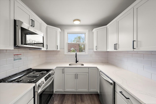 kitchen with stainless steel appliances, a sink, backsplash, white cabinetry, and dark wood finished floors