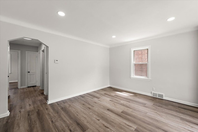 empty room with arched walkways, baseboards, wood finished floors, recessed lighting, and ornamental molding
