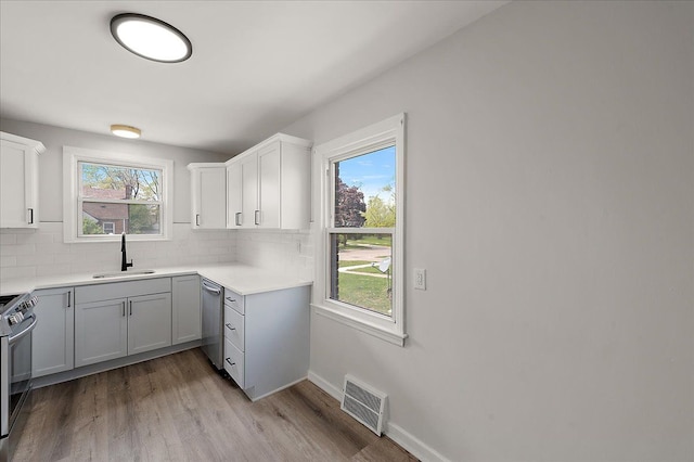 kitchen featuring a sink, stainless steel appliances, backsplash, light wood-type flooring, and white cabinetry