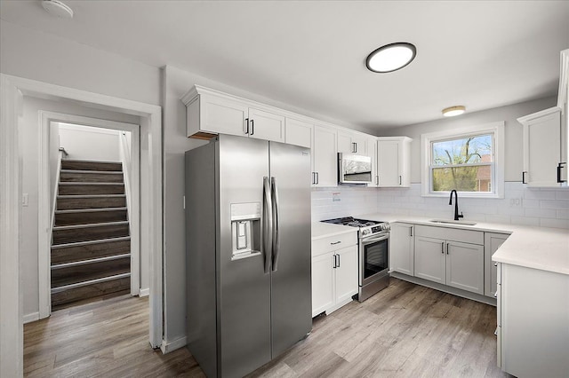 kitchen featuring stainless steel appliances, a sink, decorative backsplash, and light wood finished floors