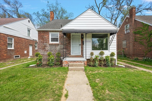 bungalow-style home with a front lawn, a chimney, roof with shingles, brick siding, and a porch