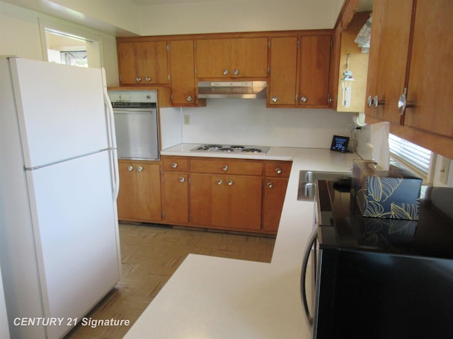 kitchen with freestanding refrigerator, oven, under cabinet range hood, and brown cabinetry