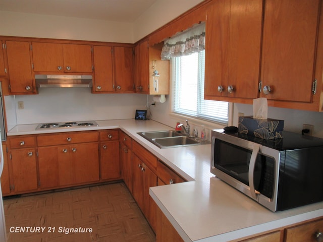 kitchen with under cabinet range hood, a sink, electric cooktop, light countertops, and brown cabinetry