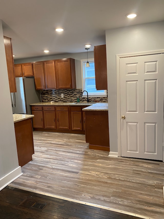 444 E Maplehurst St, Ferndale, MI 48220 - kitchen featuring brown cabinets, freestanding refrigerator, light wood-style floors, decorative backsplash, and light stone counters