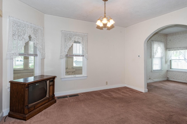 carpeted empty room featuring arched walkways, a chandelier, and baseboards