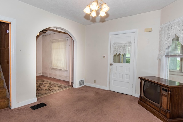 carpeted foyer with arched walkways, a chandelier, and baseboards