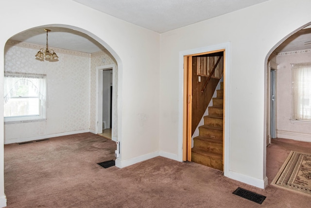 carpeted spare room featuring baseboards, a chandelier, stairs, and arched walkways