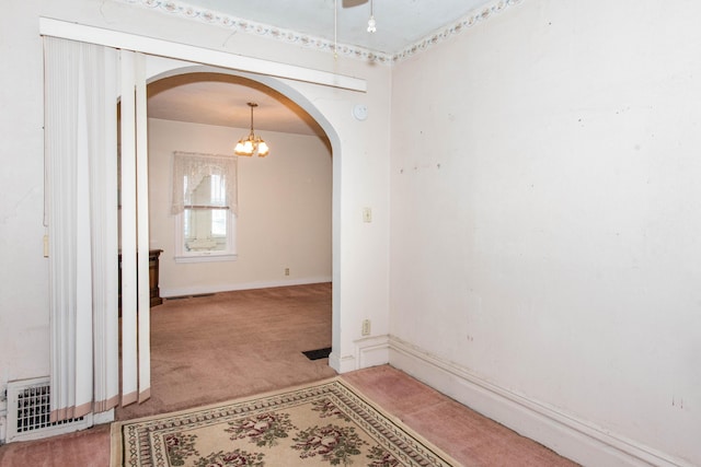 spare room featuring arched walkways, light carpet, a chandelier, and baseboards