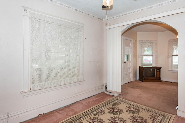 empty room with arched walkways, carpet flooring, ceiling fan, and baseboards