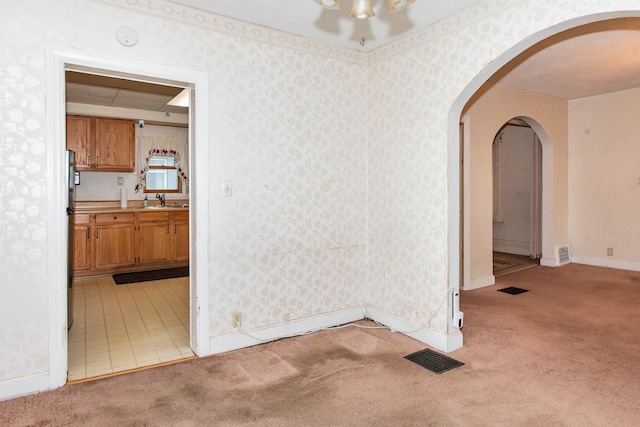 empty room with light carpet, arched walkways, a sink, baseboards, and wallpapered walls