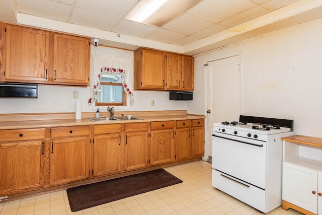 kitchen featuring white gas stove, a drop ceiling, a sink, brown cabinetry, and light countertops
